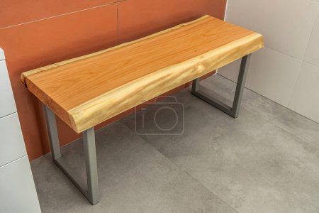 Bench with live edge wood top and gray metal legs in modern design in contemporary bathroom with concrete and terracotta tiles