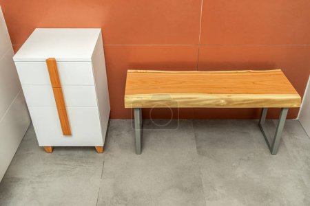 Live edge wooden bench with gray metal legs and white chest of drawers with wooden handles and legs in bathroom