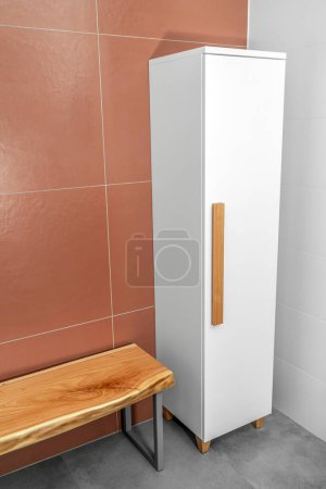 Live edge wooden bench with gray metal legs and white wardrobe with wooden handles and legs in bathroom