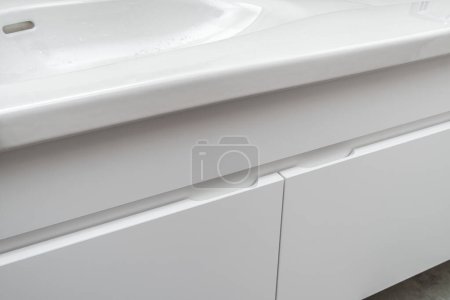 Wandschrank mit Waschtisch aus weißem Porzellan und silbernem Sensor-Wasserhahn im modernen Badezimmer mit Beton- und Holzfliesen in Nahaufnahme