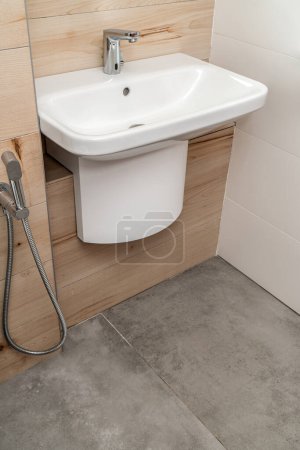 Wandwaschbecken aus weißem Porzellan mit silbernem Sensor-Wasserhahn im modernen Badezimmer mit Beton- und Holzfliesen
