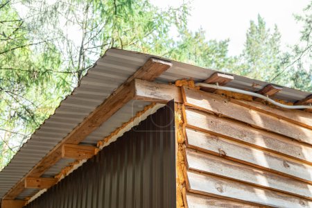 Cabane construite avec des planches de bois non finies et des tôles ondulées avec isolation en mousse, située dans une zone boisée