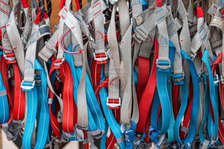 Photo for Multiple climbing harnesses in red, blue, and gray hues, hanging and ready for use, as background - Royalty Free Image