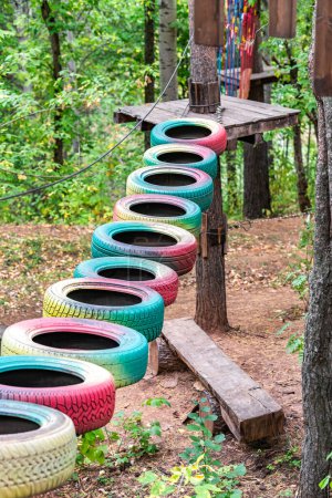 Aufgehängter Pfad aus bunten Reifen, der zwischen Bäumen in einem Abenteuer-Seilpark für körperlich anstrengende Aktivitäten in der Waldumgebung verbunden ist
