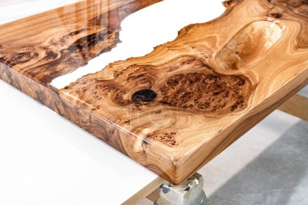 Live edge elm burl slab table top with central epoxy resin river on sawhorses in professional workshop close view