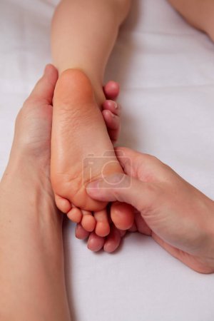 Gros plan des mains du médecin professionnel effectuant un massage pédiatrique des pieds pour améliorer la circulation sanguine dans le corps de l'enfant