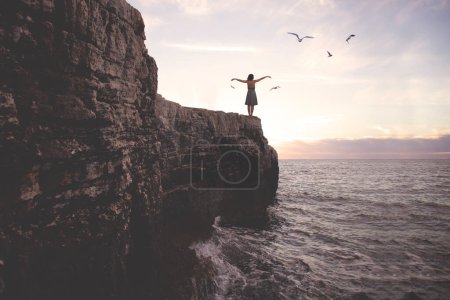 Foto de Mujer surrealista con los brazos extendidos por encima de un acantilado frente a un paisaje espectacular - Imagen libre de derechos