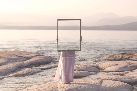 Téléchargez les photos : Femme tenant un cadre qui reflète survraiment le paysage, concept abstrait - en image libre de droit