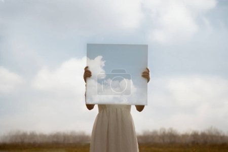 Téléchargez les photos : Gros plan d'une femme tenant une peinture surréaliste du ciel devant son visage, concept abstrait - en image libre de droit