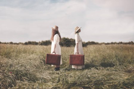 Foto de Dos viajeras surrealistas vestidas igual con maleta hombro a hombro dejan para dos destinos opuestos, concepto abstracto - Imagen libre de derechos