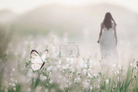 Foto de Una mariposa blanca vuela libre en medio de un prado florido mientras una mujer camina en el fondo, concepto abstracto - Imagen libre de derechos
