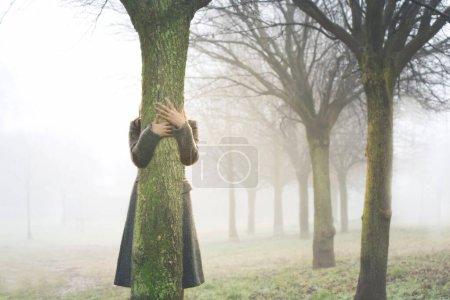 manos tocan el tronco de un árbol, abrazándolo en una arboleda rodeada de niebla