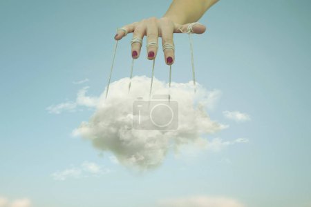 mano sosteniendo una nube atrapada entre hilos transformándola en una marioneta, concepto abstracto