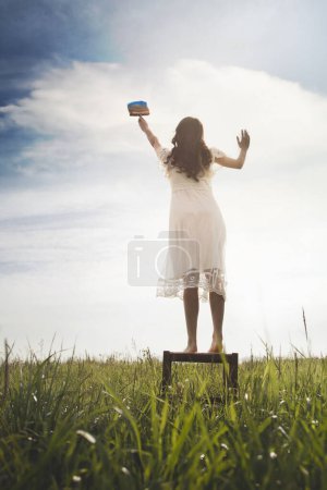 Photo for Surreal moment of a woman on a stool painting the sky with her paintbrush, abstract concept - Royalty Free Image