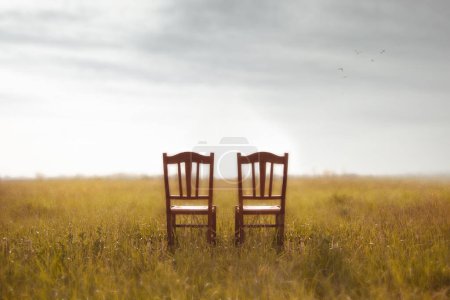 two abandoned chairs in the middle of a meadow, concept of waiting and love of a couple