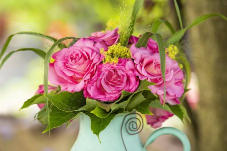 Téléchargez les photos : Bouquet de fleurs de roses dans une vieille cruche en émail dans un jardin - en image libre de droit