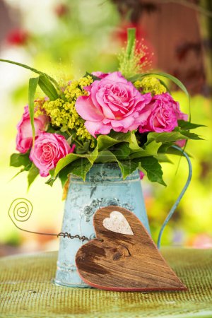 Photo for Roses flower bouquet in a old enamel jug with a wooden heart - Royalty Free Image