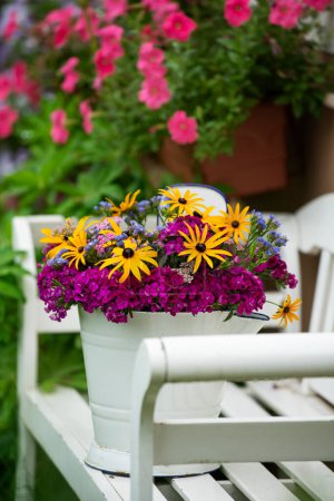 Photo for Colorful summer flowers in a enamel bucket on a garden bench - Royalty Free Image