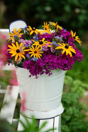 Foto de Coloridas flores de verano en un cubo de esmalte en un banco de jardín - Imagen libre de derechos