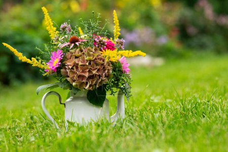 Téléchargez les photos : Bouquet de fleurs colorées dans un pot d'émail dans une prairie - en image libre de droit