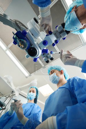 Close-up photo of doctors in protective suits and masks holding medical instrument and perform an operation