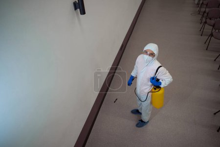 Photo for Determined cleaning service employee in protective outfit looking up at the camera while getting ready to sanitize the building - Royalty Free Image