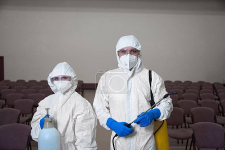 Photo for Waist-up photo of two cleaners in overall protection suits and goggles posing with cleaning equipment - Royalty Free Image