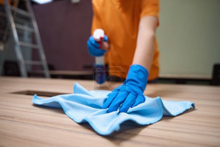 Téléchargez les photos : Plan recadré de nettoyant dans des gants en caoutchouc à l'aide d'un désinfectant pulvérisé et d'un chiffon pour nettoyer la surface - en image libre de droit
