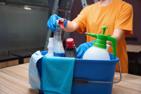 Fragment photo of janitor in bright shirt organizing the box with cleaning supplies
