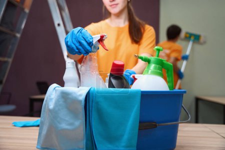 Photo for Cropped photo of pleasant young lady taking a disinfectant spray out of box with housecleaning tools - Royalty Free Image