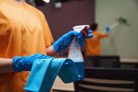 Cropped photo of cleaner wearing gloves and holding spray bottle and cloth for wiping