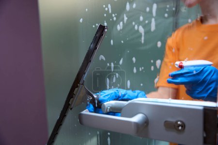 Téléchargez les photos : Photo recadrée de nettoyant professionnel pulvérisant désinfectant sur le verre et l'essuyant propre - en image libre de droit