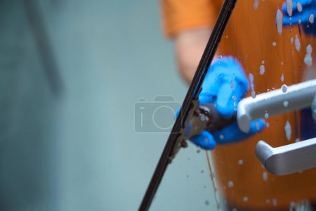 Foto de Foto recortada de una persona no reconocida en uniforme naranja usando herramientas de limpieza de ventanas para lavar el vidrio - Imagen libre de derechos