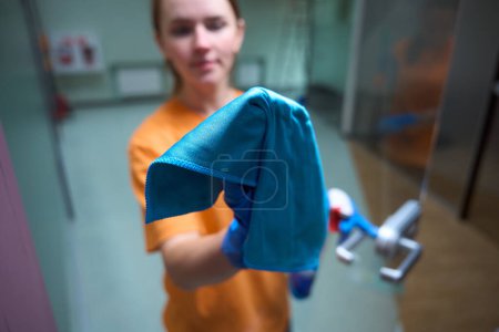 Photo for Selective focus photo of female representative of cleaning company using cloth to wipe the glass door - Royalty Free Image