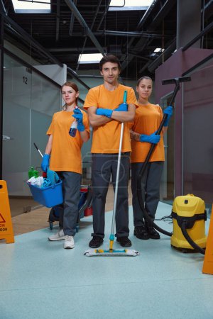 Photo for Awesome team of cleaning specialists with equipment in hands standing together and looking at the camera - Royalty Free Image