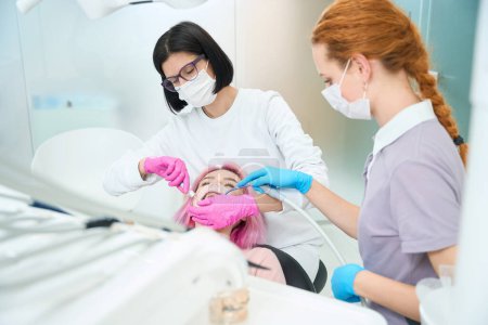 Photo for Woman dentist performs a dental procedure to a young patient, an assistant helps the doctor - Royalty Free Image