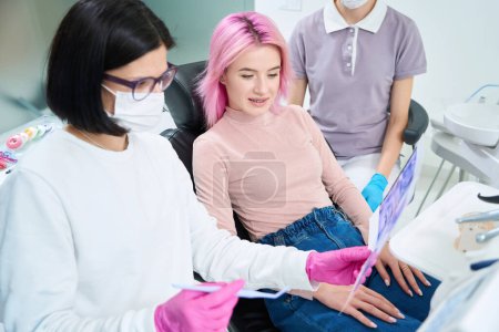 Photo for Young woman is looking at pictures of her teeth with her orthodontist, an assistant is nearby - Royalty Free Image