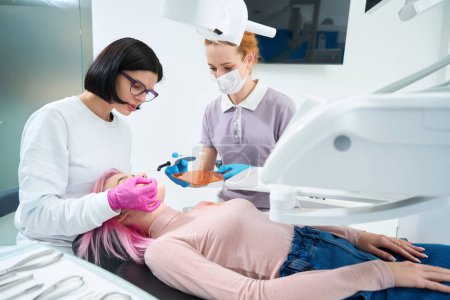 Foto de Mujer con pelo rosa en la recepción del ortodoncista, el médico trabaja con un asistente, utiliza herramientas especiales - Imagen libre de derechos