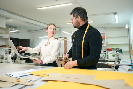 Foto de Tailor se para en una mesa de cortar y se comunica con una mujer gerente de trabajo, que utilizan un ordenador portátil - Imagen libre de derechos