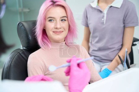 Foto de Mujer de pelo rosado sonríe afablemente al médico, se siente cómoda en la recepción - Imagen libre de derechos
