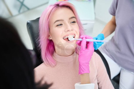Photo for Smiling female patient at the dentist, the doctor examines her bracket system - Royalty Free Image
