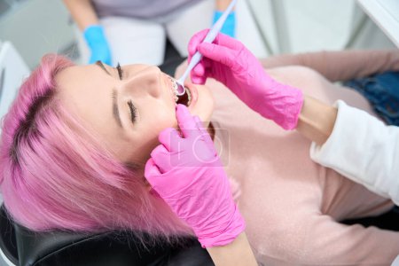 Téléchargez les photos : Spécialiste orthodontiste dans une clinique moderne utilise un miroir dentaire spécial lors de l'examen des dents d'un patient - en image libre de droit