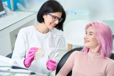 Photo for Woman orthodontist and her patient are cute chatting in the dental office, the doctor demonstrates the mock-up of the dentition - Royalty Free Image