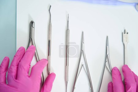 Téléchargez les photos : Les instruments dentaires en métal reposent sur une surface légère, le médecin les touche dans des gants de protection - en image libre de droit