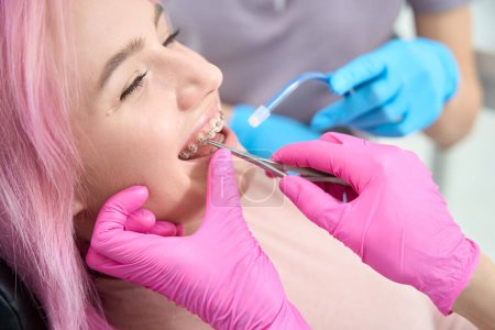 Téléchargez les photos : Jeune patiente sourit à une réception à l'orthodontiste, les spécialistes utilisent un irrigateur et des outils spéciaux - en image libre de droit