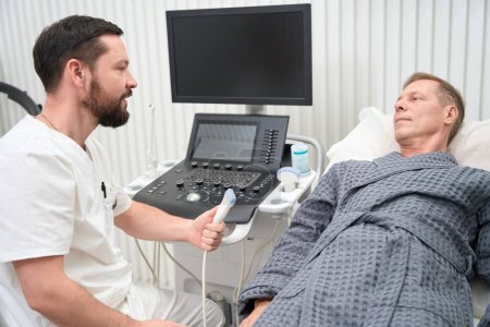 Foto de Attentive medical doctor having a conversation with patient about how ultrasound therpay works - Imagen libre de derechos