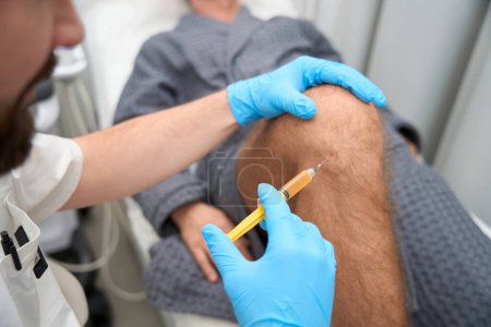 Foto de Cropped photo of medical doctor sampling biopsy from patient knee with a syringe - Imagen libre de derechos