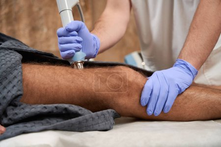 Foto de Cropped photo of doctor in medical gloves performing radiofrequency therapy on patient in order to reduce pain - Imagen libre de derechos