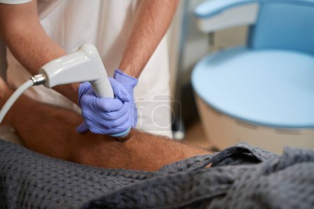 Foto de Cropped photo of medical clinic staffmember pressing radiofrequency device probe to patient knee - Imagen libre de derechos