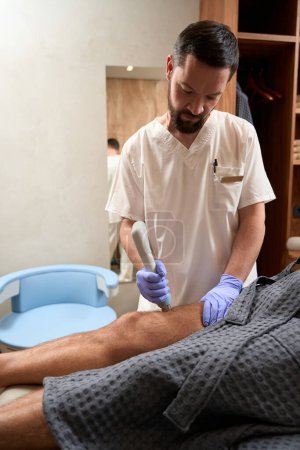 Foto de Waist-up photo of serious-looking medic operating a targeted radiofrequency therapy machine for reducing pain and muscle tension - Imagen libre de derechos